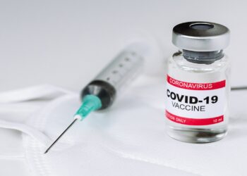 Vial with vaccine against coronavirus COVID-19 and syringe on a protective face mask. Healthcare and medical concept