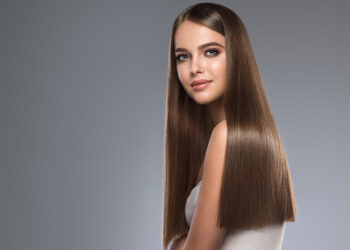 Young and pretty woman with soft smile on the face in demonstrating perfectly looking, dense and straight shiny hair. Natural gloss of healthy hair. Hair care and hairdressing art.