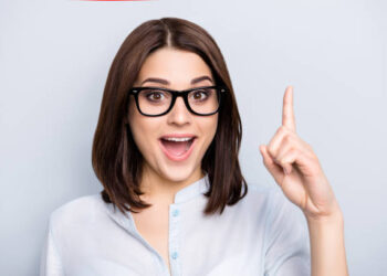 Close up portrait of pretty, charming, glad woman in shirt, eyewear finding an idea, resolution, showing index finger up with open mouth, isolated on grey background